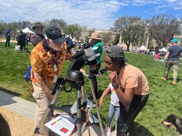 Kayla Pate and her 4-year-old daughter, Amallah Lewis, peer through the lens of a special telescope provided by the National Air and Space Museum. (AP Photo/Christina Larson)