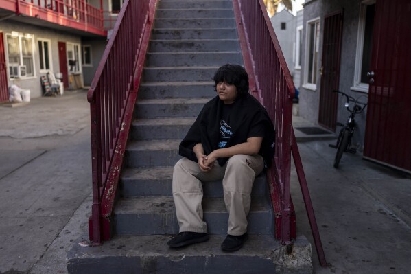 Deneffy Sánchez, 15, sits for a photo in front of a studio apartment his family shares with a retiree originally from El Salvador in Los Angeles, Tuesday, Aug. 29, 2023. (AP Photo/Jae C. Hong)