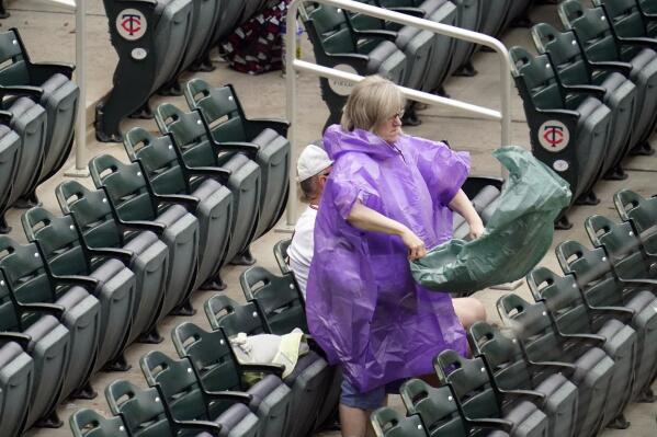 A fan shakes out a rain cover as she prepares fold up it up before leaving the ballpark as the Minnesota Twins baseball game against the Cleveland Indians was postponed, Saturday, June 26, 2021, in Minneapolis, due to heavy rain forecast in the area for much of the day. (AP Photo/Jim Mone)