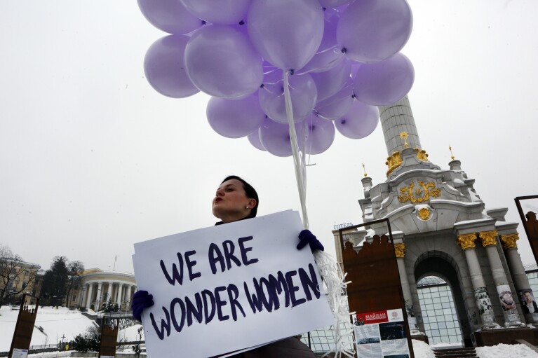 FILE - A woman holds balloons and a poster to mark International Women's Day in central Kiev, Ukraine, March 8, 2018. Women across the world will demand equal pay, reproductive rights, education, justice and other essential needs during demonstrations marking International Women’s Day on Friday, March 8, 2024. (AP Photo/Efrem Lukatsky, File)