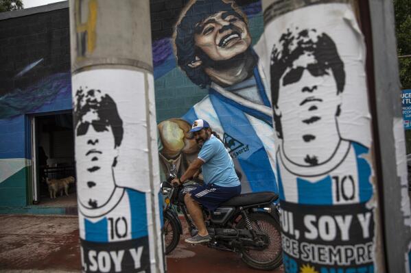 A fan prepares to ride off in his motorcycle next to a mural depicting late soccer star Diego Maradona outside the "Estrella de Fiorito" club, his first club, in the Fiorito neighborhood of Buenos Aires, Argentina, Thursday, Nov. 25, 2021, on the one-year anniversary of the soccer legend's death. (AP Photo/Rodrigo Abd)