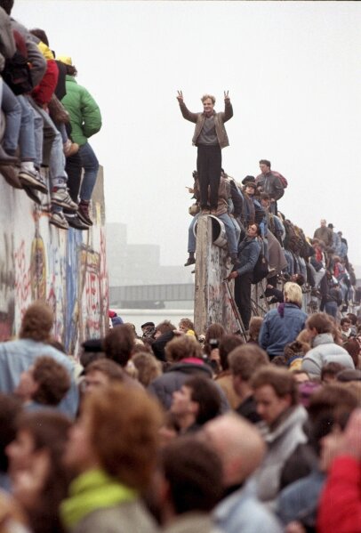 FILE - In this Sunday Nov. 12, 1989 file photo, Berliners celebrate on top of the wall as East Germans (backs to camera) flood through the dismantled Berlin Wall into West Berlin at Potsdamer Platz in Berlin. (AP Photo/Lionel Cironneau, File)