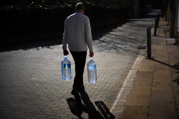 FILE - Joan Torrent, 64, walks toward his house carrying two plastic jugs of water refilled at a natural spring in Gualba, about 50 km, (31 miles) northwest of Barcelona, Spain, Wednesday, Jan 31, 2024. Spain’s Catalonia region will ease restrictions on water use for a wide area including Barcelona after recent rainfall palliated a prolonged drought, regional authorities said Tuesday, May 7, 2024. (AP Photo/Emilio Morenatti, File)