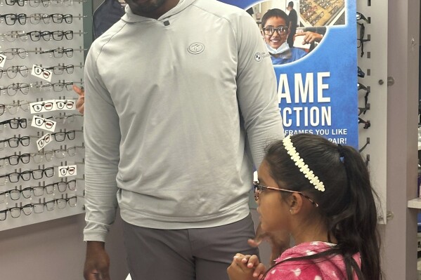 Von Miller helps a young girl pick out two pairs of frames for her eyeglasses, as part of Miller's charity, Von's Vision, which provides free eye exams and glasses for underprivileged children, on Wednesday, May 28, 2025, in Commerce City, Colo. (AP Photo/Arnie Stapleton)