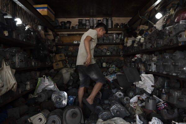 Tu Chi Vy tiptoes through his shop packed with refurbished motors in Nhat Tao Market, the largest informal recycling market in Ho Chi Minh City, Vietnam, on Monday, Jan. 29, 2024. (AP Photo/Jae C. Hong)