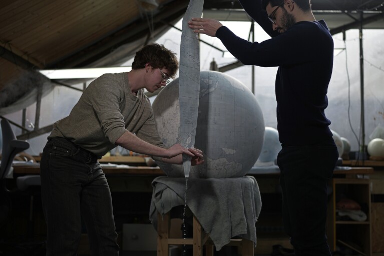 Artists make a globe at a studio in London, Tuesday, Feb. 27, 2024. Globes in the age of Google Earth capture the imagination and serve as snapshots of how the owners see the world and their place in it. Peter Bellerby made his first globe for his father, after he could not find one accurate or attractive enough. In 2008, he founded Bellerby & Co. Globemakers in London. His team of dozens of artists and cartographers has made thousands of bespoke globes up to 50 inches in diameter. The most ornate can cost six figures. (AP Photo/Kin Cheung)