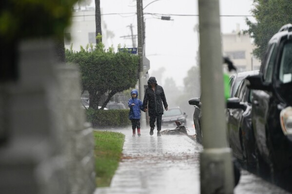 People walk in the rain, Sunday, Aug. 20, 2023, in Los Angeles. Tropical Storm Hilary swirled northward Sunday just off the coast of Mexico's Baja California peninsula, no longer a hurricane but still carrying so much rain that forecasters said 
