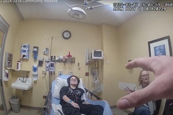 In this frame grab taken from body camera video provided by the Owasso, Okla., Police Department, an officer, hand at right, speaks to 16-year-old Nex Benedict, left, and their mother, Sue Benedict, at a hospital, Wednesday, Feb. 7, 2024. Sue says that Nex was knocked to the floor during a fight in a school bathroom earlier in the day. Nex died the following day. (Owasso Police Department via AP)