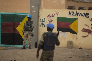 FILE - United Nations peacekeepers stand guard at the entrance to a polling station covered in separatist flags and graffiti supporting the creation of the independent state of Azawad, in Kidal, Mali on July, 27, 2013. United Nations peacekeepers started departing from two bases in northern Mali Monday Oct. 16, 2023 as part of a forced withdrawal from the country amid increasing insecurity and a rise in attacks by Islamic extremists. (AP Photo/Rebecca Blackwell, File)