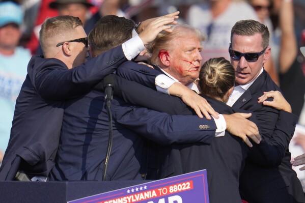 Republican presidential candidate former President Donald Trump is surrounded by U.S. Secret Service agents as he is helped off the stage at a campaign rally in Butler, Pa., Saturday, July 13, 2024. (AP Photo/Gene J. Puskar)