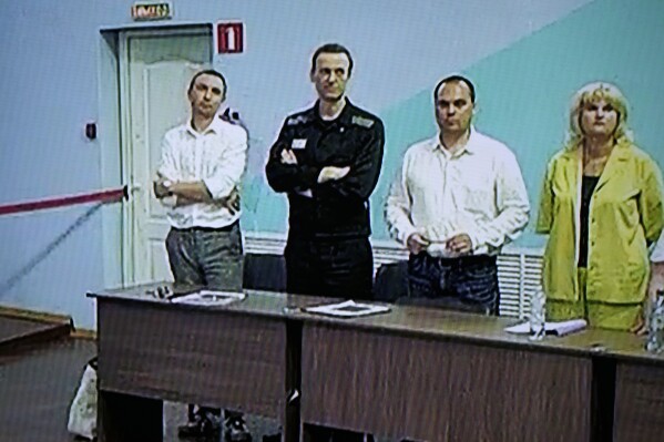 Russian opposition leader Alexei Navalny, 2nd left, is seen on a TV screen standing among his lawyers, as he appears in a video link provided by the Russian Federal Penitentiary Service, during a hearing in the colony, in Melekhovo, Vladimir region, about 260 kilometers (163 miles) northeast of Moscow, Russia, on Friday, Aug. 4, 2023. Navalny on Friday was convicted on extremism charges and sentenced to 19 years in prisons, in the harshest ruling against the imprisoned Kremlin critic to date. (AP Photo/Alexander Zemlianichenko)