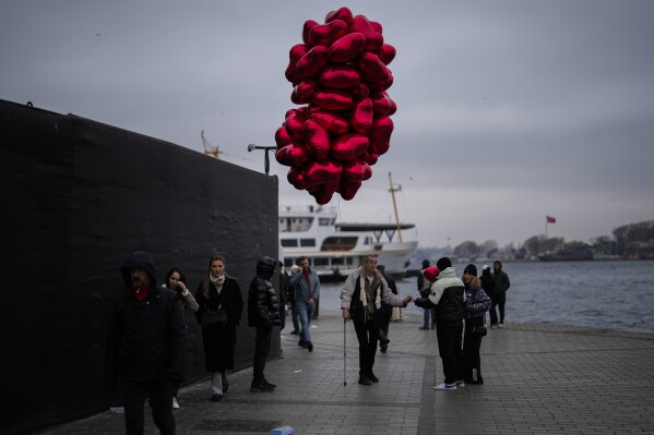 A man sells a heart shaped balloon to a couple next to the Bosphorus during Valentine's Day in Istanbul, Turkey, Wednesday, Feb. 14, 2024. (AP Photo/Francisco Seco)