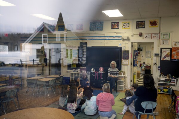 Teacher Diane Nicholls leads her class of first through third graders at the Elmore School, the last one-room schoolhouse in the state, Wednesday, March 6, 2024, in Elmore, Vt., as the town hall is reflected in the window at left.  (AP Photo/David Goldman)