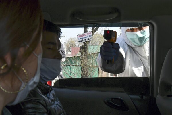 In this Wednesday, March 25, 2020, photo, a medical worker checks temperatures of a car passengers at a checkpoint near Bishkek, Kyrgyzstan. For most people, the new coronavirus causes only mild or moderate symptoms. For some it can cause more severe illness. (AP Photo/Vladimir Voronin)