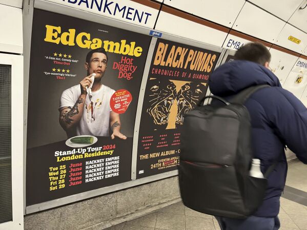A view of a poster advertising comedian Ed Gamble's Hot Diggity Dog tour on the Bakerloo line platform at Embankment underground station in London, Wednesday March 27, 2024. Gamble has been ordered to change a subway station poster campaign for his new standup show because the image of a hot dog violated the transit network’s ban on junk food advertising. The poster for the show, “Hot Diggity Dog,” showed a mustard- and ketchup-smeared Gamble beside a half-eaten hot dog on a plate. A bemused Gamble replaced the wiener with a cucumber, and the poster was approved. (Joe Sene/PA via AP)