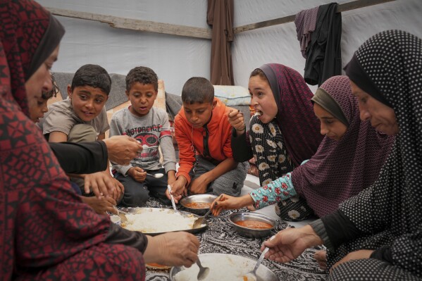 The Al-Najjar family eats peas with rice in their family tent in Muwasi, on the outskirts of Khan Younis in the southern Gaza Strip, Friday, April, 25, 2025. (AP Photo/Abdel Kareem Hana)
