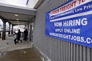 FILE - In this Dec. 10, 2020, file photo, a "Now Hiring" sign hangs on the front wall of a Harbor Freight Tools store in Manchester, N.H. The latest figures for jobless claims, issued Thursday, Jan. 14, 2021 by the Labor Department, remain at levels never seen until the virus struck.  (AP Photo/Charles Krupa, File)