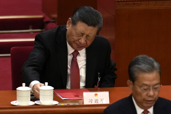 Chinese President Xi Jinping, rear, reacts after drinking from a cup at the closing session of the National People's Congress held at the Great Hall of the People in Beijing, Monday, March 11, 2024. (AP Photo)
