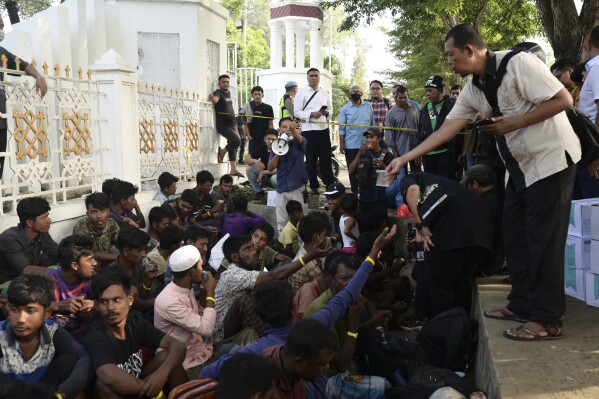 A local official distributes water to Rohingya refugees outside the governor's office in Banda Aceh, Indonesia, Monday, Dec. 11, 2023. Two boats carrying hundreds of Rohingya Muslims, including emaciated women and children, arrived on Sunday at Indonesia's northernmost province of Aceh where they faced rejection from local communities who are protesting against the increasing numbers of refugees that have entered the region over the past few weeks. (AP Photo/Reza Saifullah)