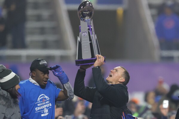 Boise State head coach Spencer Danielson celebrates with safety Seyi Oladipo, the defensive player of the game, with the Championship Trophy after their matchup against UNLV in the Mountain West Championship NCAA college football game Friday, Dec. 6, 2024, in Boise, Idaho. (AP Photo/Steve Conner)