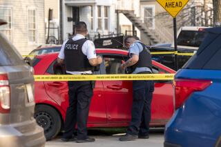 Chicago police officers secure a red car that crashed into a fence in the 4500 block of South Marshfield Avenue that is suspected to be related to a fatal shooting Tuesday, May 10, 2022 in Chicago. The Associated Press on Friday, Aug. 4, 2023, reported on social media posts falsely claiming that a new law in Illinois allows any immigrant living in the country illegally to become a police officer.
 (Tyler Pasciak LaRiviere /Chicago Sun-Times via AP)