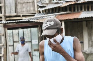 A man wearing mask against the spread of the new coronavirus coughs as he walks in the Cristo del Consuelo neighborhood of Guayaquil, Ecuador, Tuesday, April 14, 2020. The poor neighborhood of Cristo del Consuelo has been hit hard by the new coronavirus pandemic, prompting the local government to provided food and medical assistance for the residents. (AP Photo/Angel de Jesus)