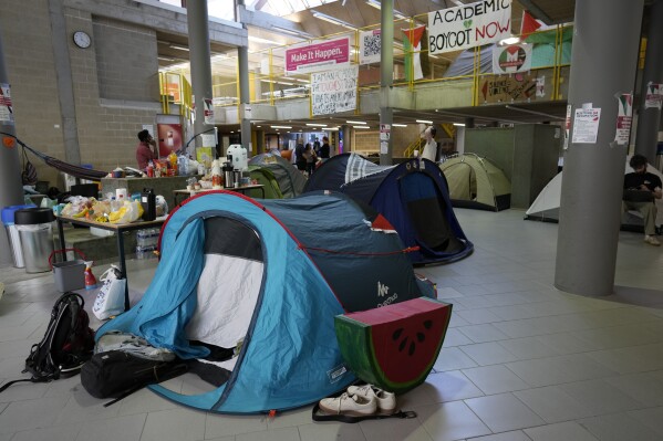 Signs and a food table are set up in a tent camp, set up by pro-Palestinian students and demonstrators at the University of Antwerp, as students occupy parts of the campus in Antwerp, Belgium, Tuesday, May 14, 2024. (AP Photo/Virginia Mayo)