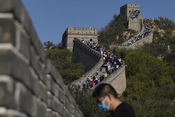 FILE - A man wearing a mask to help protect from the coronavirus stands near a stretch of the Badaling Great Wall of China on the outskirts of Beijing on Oct. 6, 2020. Authorities in China arrested the two men for smashing a path through a section of the ancient wall, a cultural icon and United Nations protected heritage site. (AP Photo/Ng Han Guan, File)