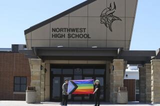 FILE - Former Viking Saga newspaper staff members Marcus Pennell, left, and Emma Smith display a pride flag outside of Northwest High School in Grand Island, Neb., July 20, 2022. A Nebraska public school district that shuttered the school’s award-winning student newspaper following its issue of an LGBTQ-focused edition has agreed to bring back the newspaper next year in digital form. (McKenna Lamoree/The Independent via AP, File)