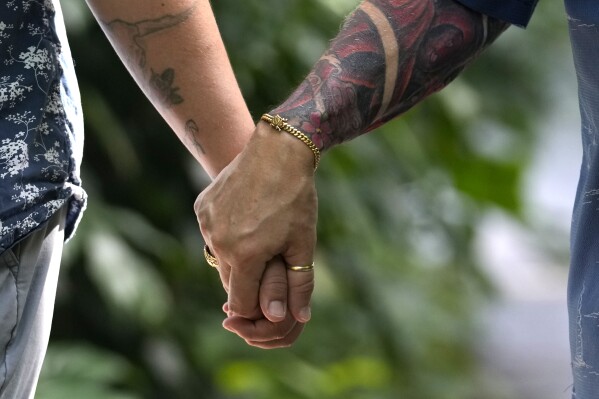 Morgan Mayfaire, a transgender man, right, holds hands with his wife, Ashley, Sunday, July 23, 2023, at Fairchild Tropical Garden in Miami. Mayfaire, 64, the executive director of TransSOCIAL, a Florida support and advocacy group, says “The community’s going to take care of itself. It’s as simple as that. We’re going to find ways to take care of ourselves and we’re going to survive this. ... And as far as trans youth panicking over this, look to your elders.”. (AP Photo/Lynne Sladky)