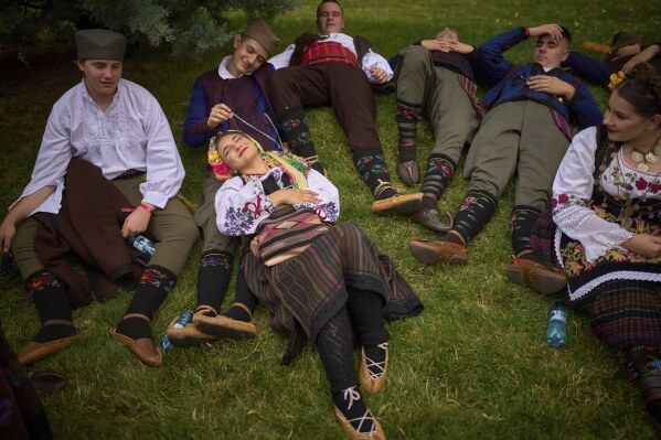 Members of a traditionial group from Serbia rest in the shade before a parade by international ensembles and those of ethnic groups from Romania showcasing traditional outfits, dances and songs, in Bucharest, Romania, Saturday, June 21, 2025. (AP Photo/Vadim Ghirda)