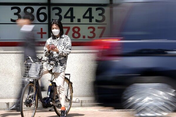 2024年5月15日，星期三，东京一家证券公司，一名骑着自行车的人停在一块显示日本日经225指数的电子股票板前。（美联社照片/尤金·胡希科）