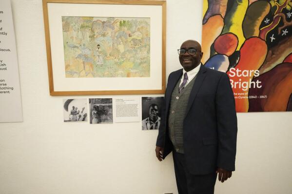 Gift Livingtsone Sango, 65, stands next to a painting by his father depicting Jesus as a Black man at the National Gallery of Zimbabwe, Thursday, July 14, 2022. The painting done by his late father in the 1940s is part of a historic exhibit, "The Stars are Bright," now showing in Zimbabwe for the first time since the collection left the country more than 70 years ago. A photograph of Sango's father, Livingstone, as a young boy hangs next to the painting. (AP Photo/Tsvangirayi Mukwazhi)
