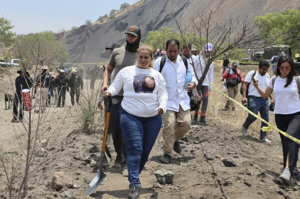 Ceci Flores, leader of a "searching mothers" group from northern Mexico, carries a shovel at the site where she said her team found a clandestine crematorium in Tlahuac, on the edge of Mexico City, Wednesday, May 1, 2024. Flores announced late Tuesday that her team had found bones around clandestine burial pits and ID cards, and prosecutors said they were investigating to determine the nature of the remains. Behind her at left is activist Bryan Lebaron. (AP Photo/Ginnette Riquelme)