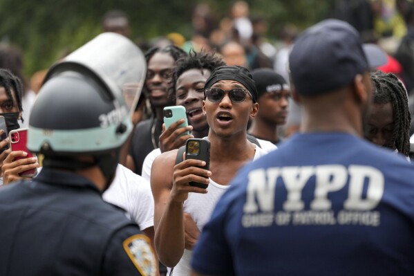 FILE - People record New York City Police Department officers as they chant anti-NYPD slogans, Aug. 4, 2023, in New York's Times Square. In New York, a proposed bill that would require officers to document basic information when they question someone has divided city government and been thrust into the national spotlight after police pulled over a black lawmaker without giving him a reason. (AP Photo/Mary Altaffer, File)