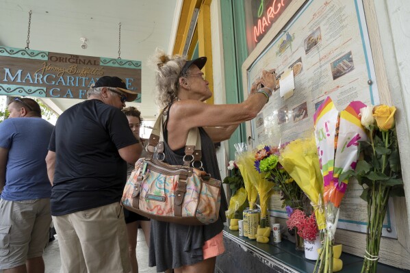In this photo provided by the Florida Keys News Bureau, Susan Hudnall pins a condolence note about Jimmy Buffett's passing to the front window of the Margaritaville Cafe in Key West, Fla., Saturday, Sept. 2, 2023, in Key West, Fla. Buffett, who popularized beach bum soft rock with the escapist Caribbean-flavored song “Margaritaville” and turned that celebration of loafing into a billion-dollar empire of restaurants, resorts and frozen concoctions, died Friday, Sept 1. He was 76. Hudnall, a visitor from Urbanna, Va, said she had seen every Buffett show in the past 20 years within a 100-mile radius of her home. (Rob O'Neal/Florida Keys News Bureau via AP)