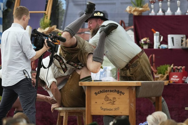 Men dressed in traditional clothes try to pull the opponent over the table at the German Championships in Fingerhakeln or finger wrestling, in Pang, near Rosenheim, Germany, Sunday, April 27, 2025. (AP Photo/Matthias Schrader)