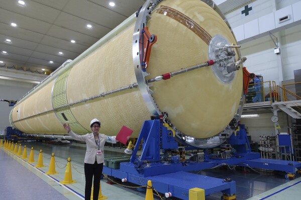 FILE - A Mitsubishi Heavy Industries staff member stands next to the top of the first stage of a H3 rocket, inside the Mitsubishi Heavy Industries' Nagoya Aerospace Systems Works Tobishima Plant in Tobishima, Aichi prefecture Thursday, March 21, 2024. Japan’s space agency announced Friday, April 26, that it will launch its new flagship rocket H3 on June 30 carrying an observation satellite for disaster response and security purposes, a key mission that it had failed in its debut flight last year.(AP Photo/Mari Yamaguchi)