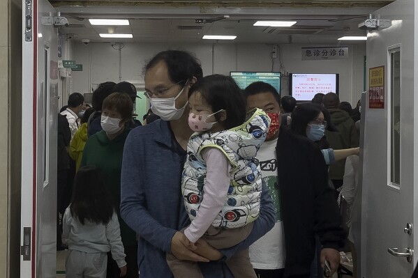 A man carriers a child walk out from a crowded holding room of a children's hospital in Beijing on Oct. 30, 2023. A surge in respiratory illnesses across China that has drawn the attention of the World Health Organization is caused by the flu and other known pathogens and not by a novel virus, the country's health ministry said Sunday, Nov. 26, 2023. (AP Photo/Andy Wong)