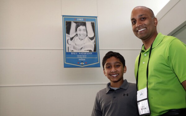 FILE - Dr. Balu Natarajan, right, from Hinsdale, Ill., poses for a photograph with his son Atman Balakrishnan, 12, at the Scripps National Spelling Bee, Tuesday, May 29, 2018, in Oxon Hill, Md. Since 1999, 28 of the last 34 Scripps National Spelling bee champions have been Indian American. And most of those winners are the offspring of parents who arrived in the United States on student or work visas. The experiences of first-generation Indian Americans and their spelling bee champion children illustrate the economic success and cultural impact of the nation’s second-largest immigrant group. (AP Photo/Alex Brandon, File)