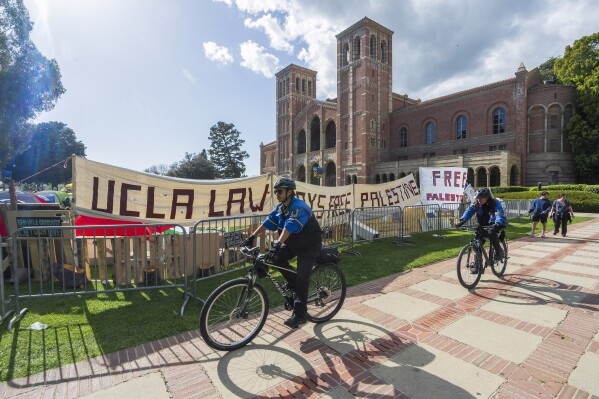 UCLA campus police cycle around the perimeter of a pro-Palestinian encampment on the UCLA campus Friday، April 26، 2024، in Los Angeles. (AP Photo/Damian Dovarganes)
