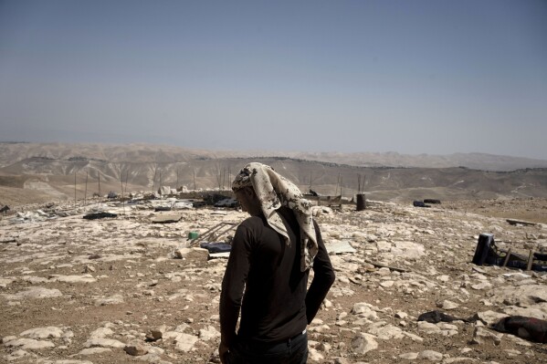 Palestinian shepherd Mustafa Arara, 24, stands in the ruins of the West Bank Bedouin village of al-Baqa where residents fled in July after settlers established an outpost a stone's throw from the village in June, Wednesday, Aug. 9, 2023. Out of 33 people who fled the Palestinian hamlet east of Ramallah, just one six-person family has returned after settlers from a newly established outpost wreaked havoc on the village, setting their sheep loose on Palestinian grazing fields and torching a home. (AP Photo/Maya Alleruzzo)
