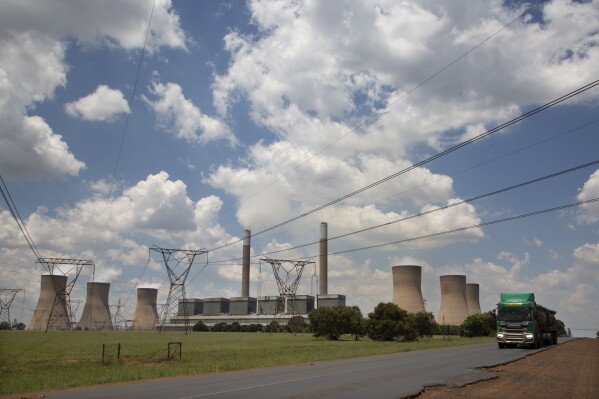 FILE — A coal truck, right, passes the coal-powered Duvha power station, near Emalahleni (formerly Witbank) east of Johannesburg, Thursday, Nov. 17, 2022. The World Bank has approved a $1 billion loan for South Africa to help it address an energy crisis that has peaked this year with the country’s worst electricity blackouts. It has forced South Africa to lean more heavily on its highly polluting coal-fired power stations. (AP Photo/Denis Farrell/File)