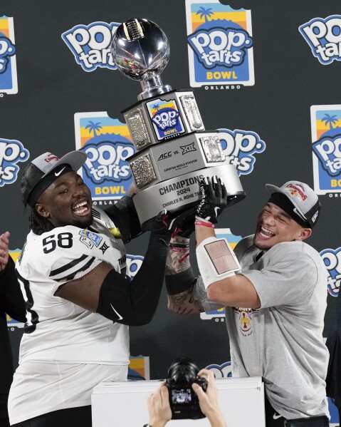 Iowa State defensive lineman J.R. Singleton (58) and wide receiver Jaylin Noel, right, hold up the championship trophy after winning the Pop Tarts Bowl NCAA college football game against Miami, Saturday, Dec. 28, 2024, in Orlando, Fla. (AP Photo/John Raoux)