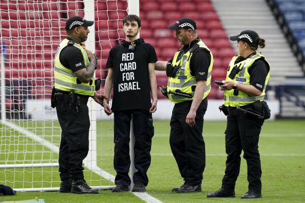 Police speak to a protestor wearing a "Red Card For Israel" T-Shirt after he chained himself to a goalpost ahead of the UEFA Women's Euro 2025 qualifying match between Scotland and Israel, at Hampden Park in Glasgow, Scotland, Friday May 31, 2024. (Jane Barlow/PA via AP)