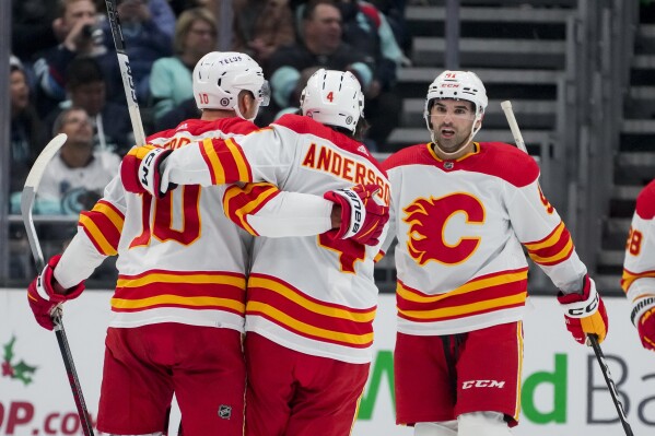 Calgary Flames center Jonathan Huberdeau (10) celebrates scoring against the Seattle Kraken as he is greeted by defenseman Rasmus Andersson and center Nazem Kadri, right, during the first period of an NHL hockey game, Monday, Nov. 20, 2023, in Seattle. (AP Photo/Lindsey Wasson)
