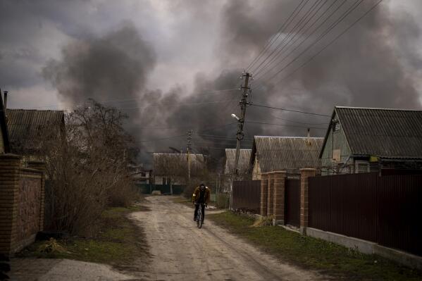 A Ukrainian man rides his bicycle near to a factory and a store burning after been bombarded in Irpin, on the outskirts of Kyiv, Ukraine, Sunday, March 6, 2022. (AP Photo/Emilio Morenatti)