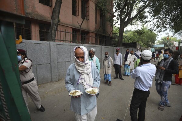 An impoverished man walks after receiving food prepared by the Bangla Sahib Gurdwara kitchen as others wait in a queue in New Delhi, India, Sunday, May 10, 2020. The Bangla Sahib Gurdwara has remained open through wars and plagues, serving thousands of people simple vegetarian food. During India's ongoing coronavirus lockdown about four dozen men have kept the temple's kitchen open, cooking up to 100,000 meals a day that the New Delhi government distributes at shelters and drop-off points throughout the city. (AP Photo/Manish Swarup)