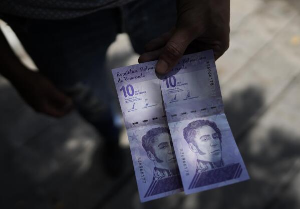 A man shows a new 10 Bolivar bank note after withdrawing it from a cash machine in Caracas, Venezuela, Friday, Oct 1, 2021. A new currency with six fewer zeros debuts Friday in Venezuela, whose currency has been made nearly worthless by years of the world's worst inflation. The new currency tops out at 100 bolivars, a little less than $25 until inflation starts to eat away at that as well. (AP Photo/Ariana Cubillos)