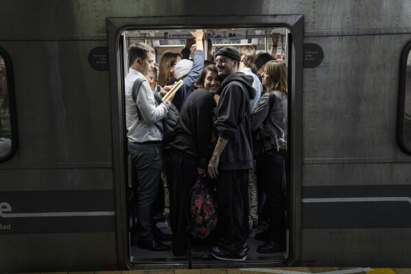 A smiling couple squeeze into a subway car packed with commuters, in Buenos Aires, Argentina, April 12, 2024. (AP Photo/Rodrigo Abd)